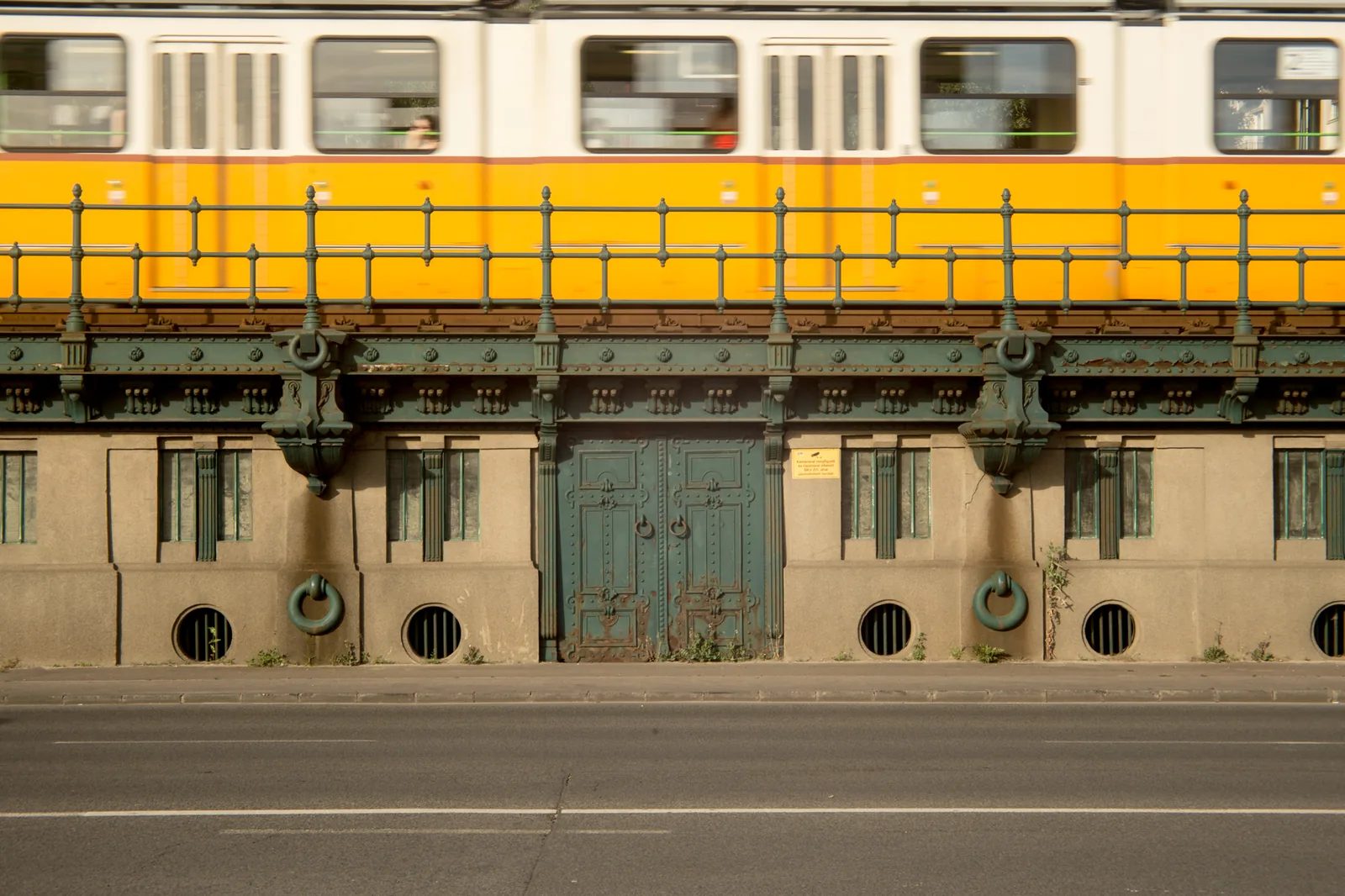 黃色電車行經鋼構橋，橋下可見門窗。