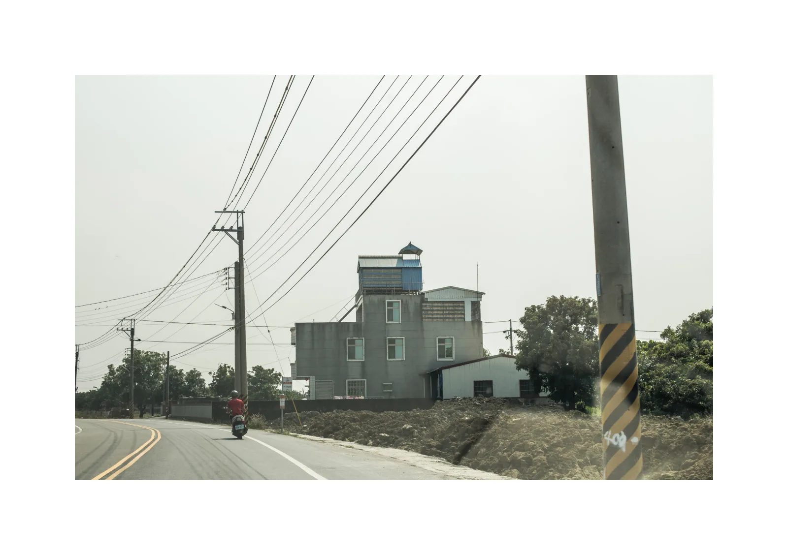 小冊子《1》第 9 頁：彎曲道路沿著電線桿前進，一名騎士經過路旁的多層建築。