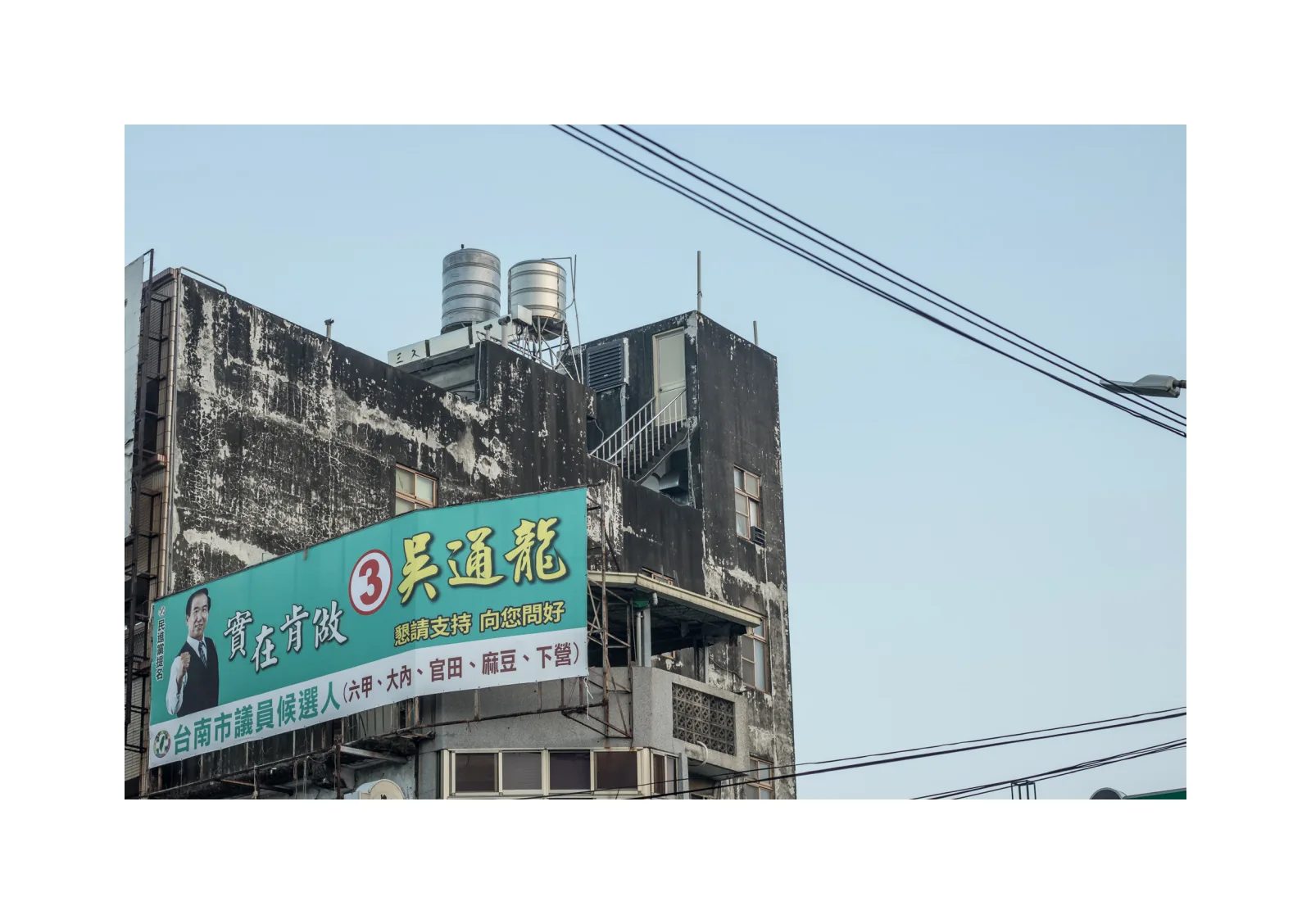 小冊子《1》第 16 頁：斑駁建築外牆掛著綠色廣告看板，屋頂可見兩個水塔。
