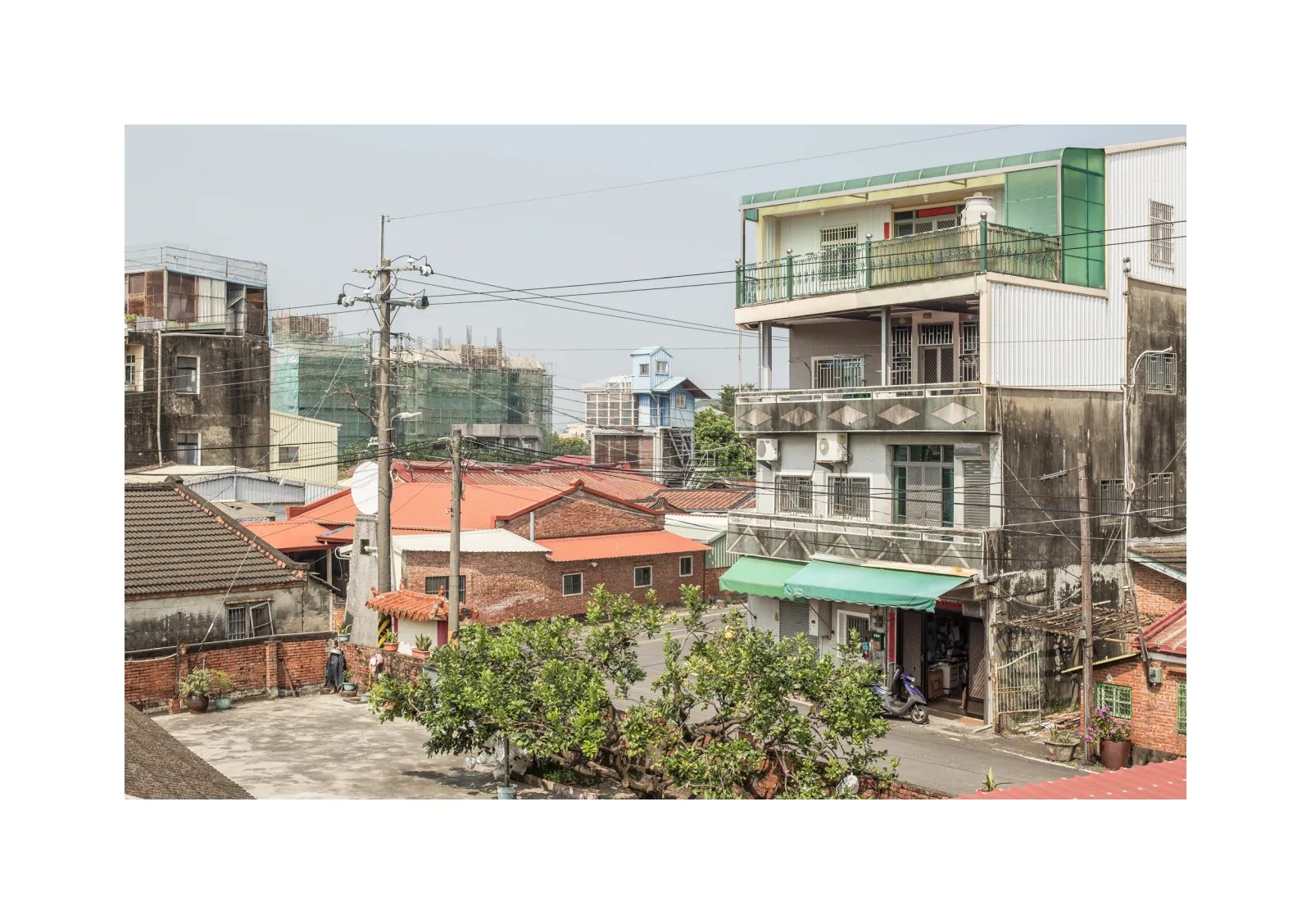 小冊子《1》第 17 頁：紅瓦平房與多層住宅相鄰，電線橫跨巷口及綠色遮棚。