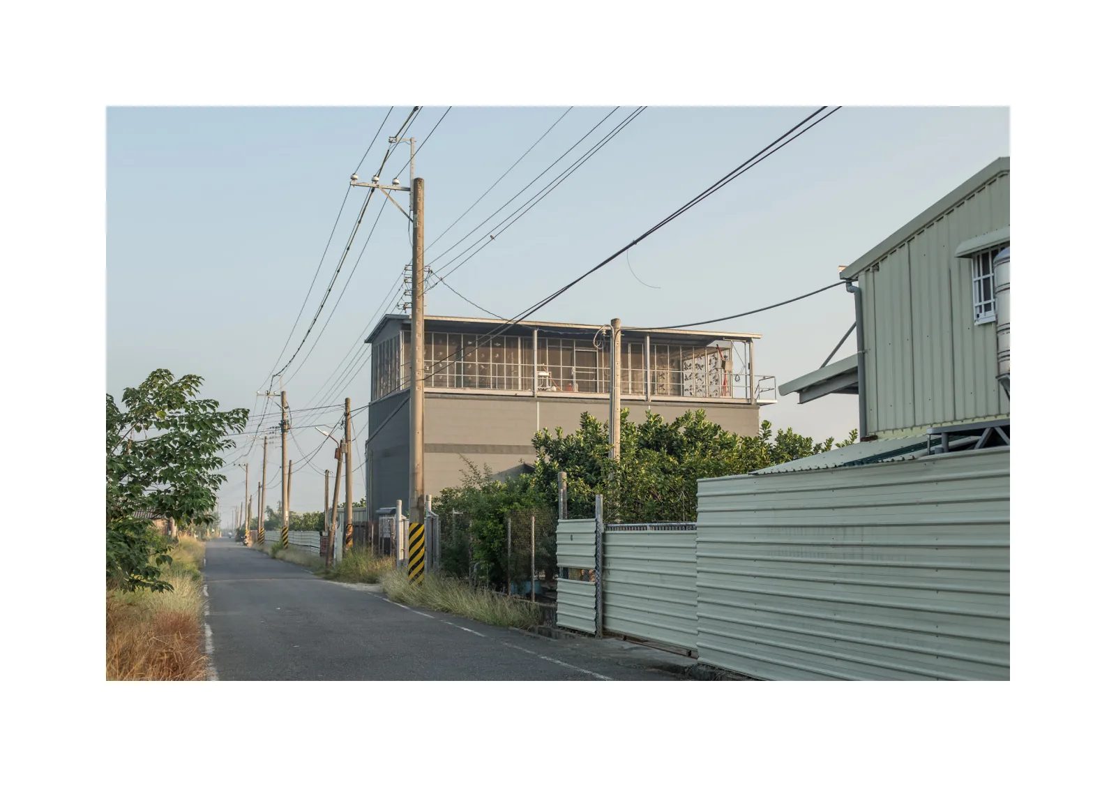 小冊子《1》第 20 頁：筆直小路沿著電線桿延伸，路旁是帶有格柵的建築與鐵皮圍籬。