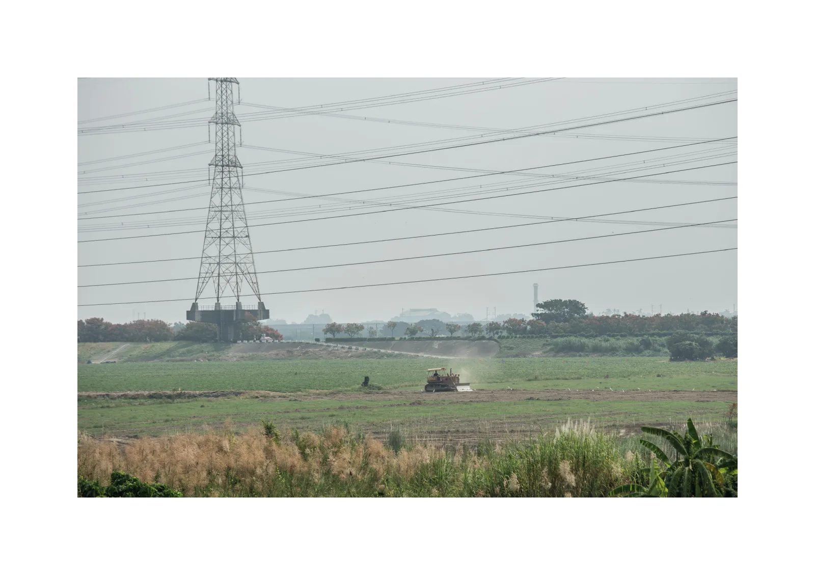 小冊子《1》第 26 頁：高壓電塔與多條電線跨過田地，一台小型農機在遠方作業。