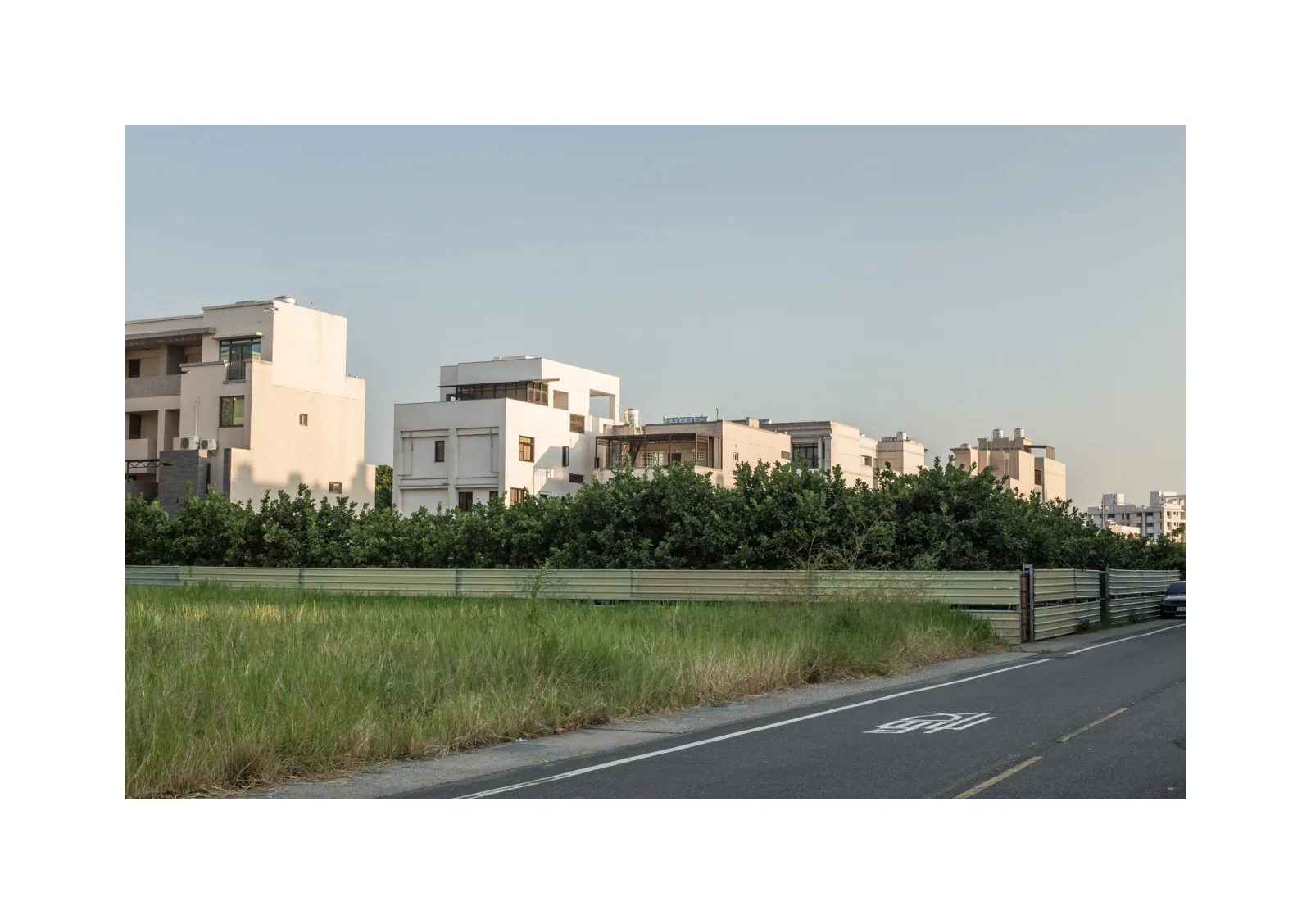 小冊子《1》第 32 頁：道路與草地前方排列淺色住宅，中間隔著一片果園。