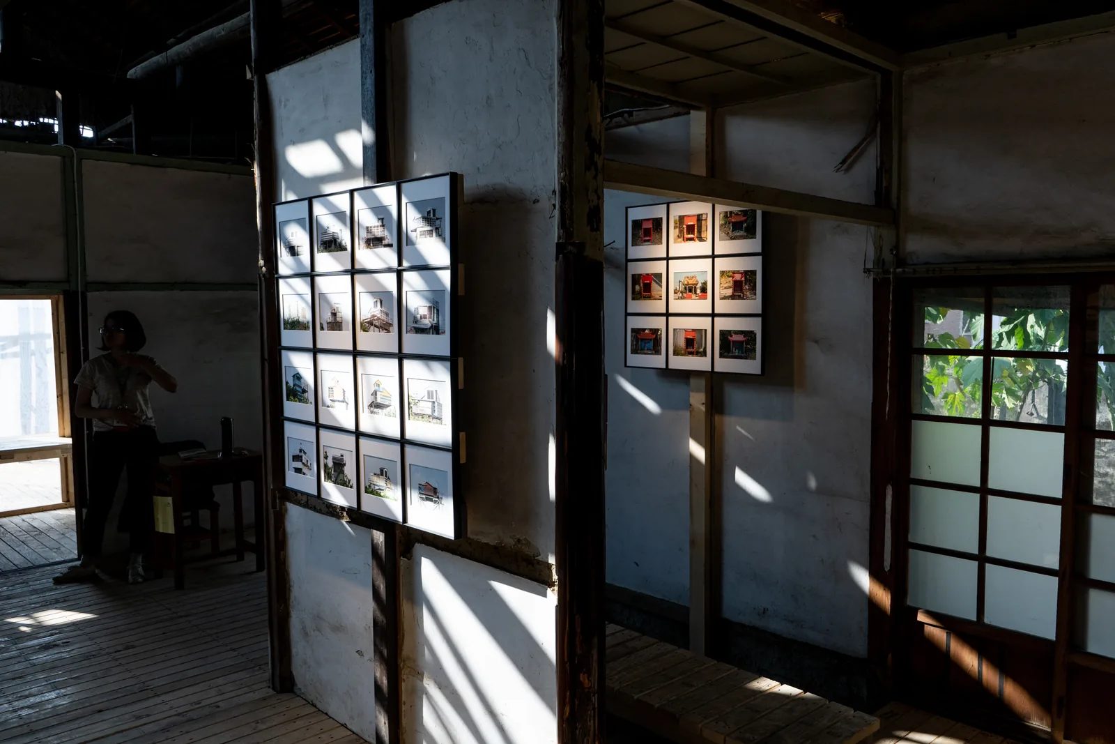 日光穿過木造展場，鴿舍與信仰主題的燈箱分掛在兩面牆上，木地板上留下窗影。